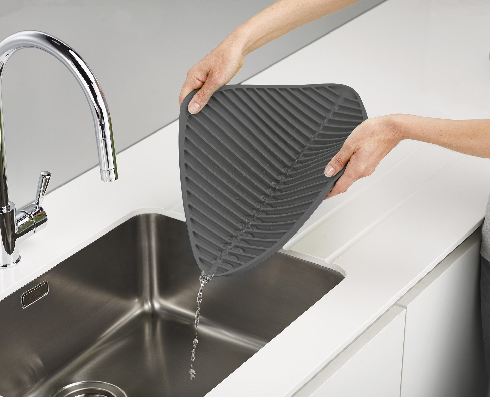Un tappetino grigio per asciugare è tenuto sopra un lavello, l'acqua scola.