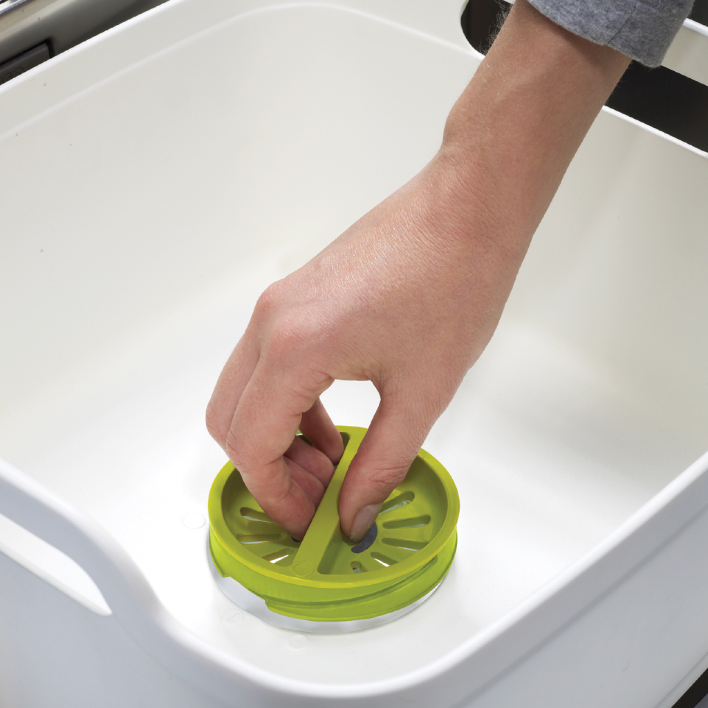 Una mano posiziona uno scolapasta verde in un lavello bianco.
