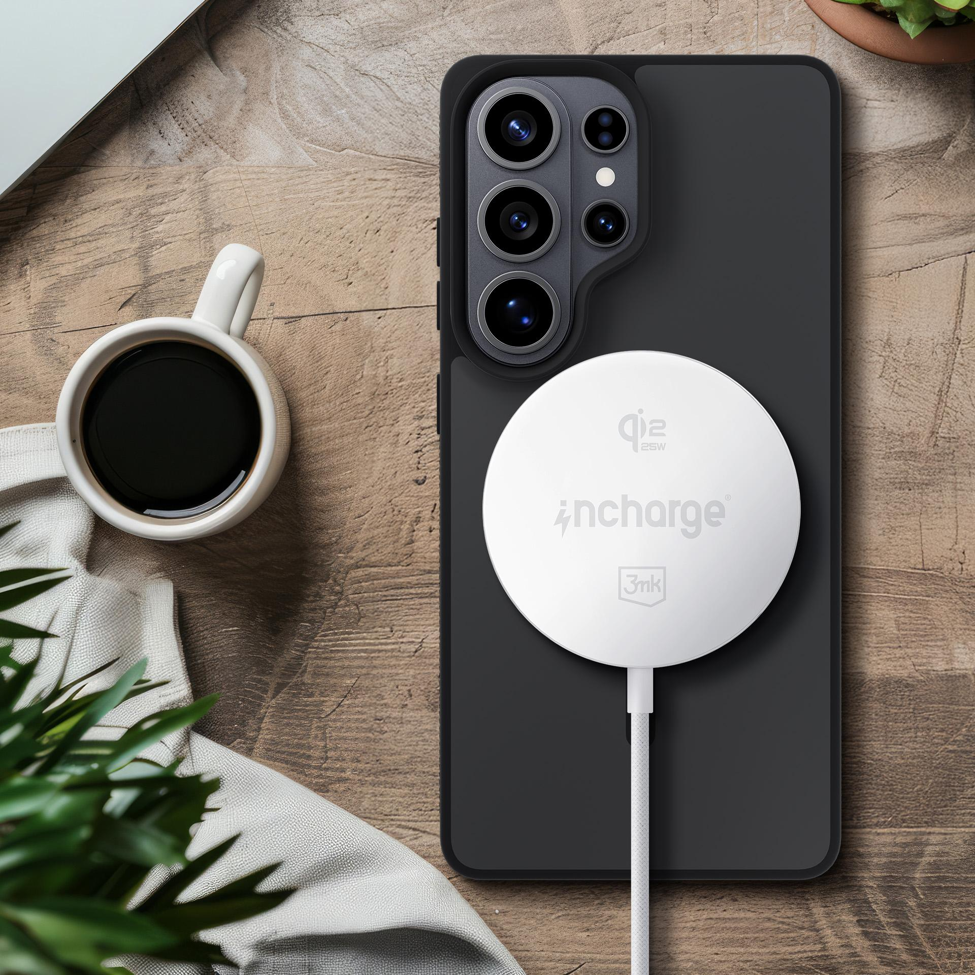 Biała ładowarka jest przymocowana do tyłu czarnego smartfona. Filiżanka kawy w pobliżu.