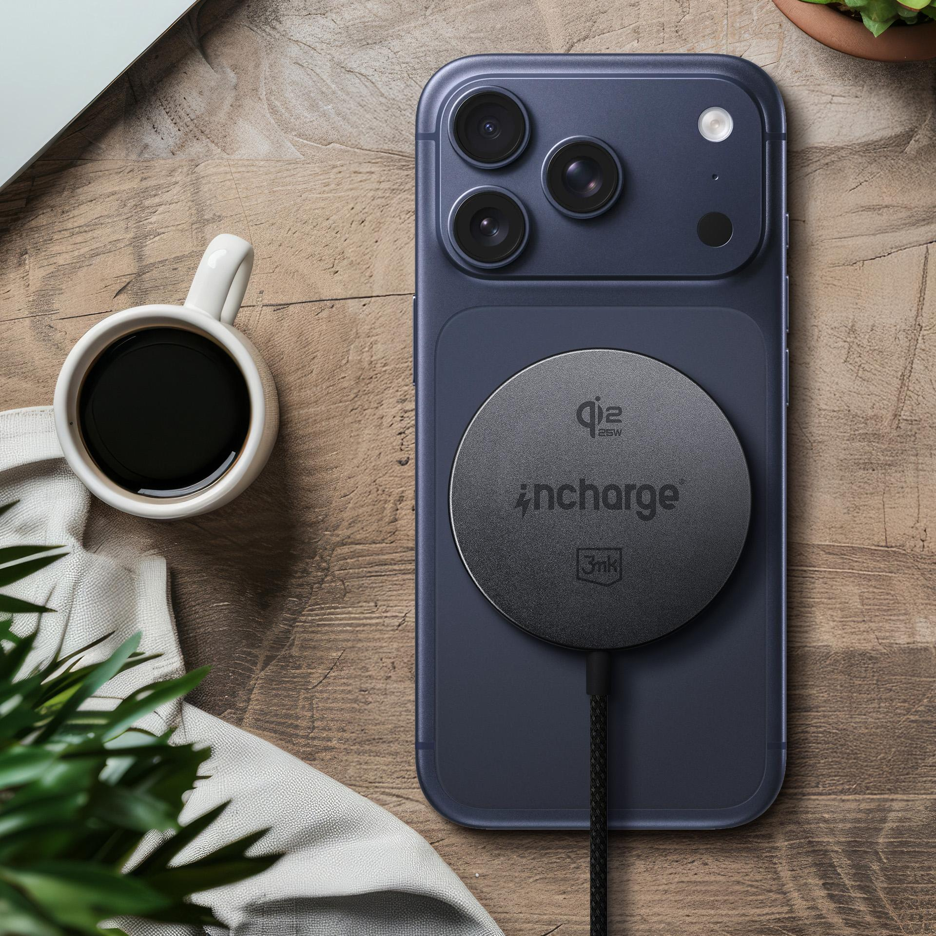 Czarny iPhone leży na drewnianym stole, z okrągłą czarną ładowarką bezprzewodową. W pobliżu znajduje się biała filiżanka kawy.