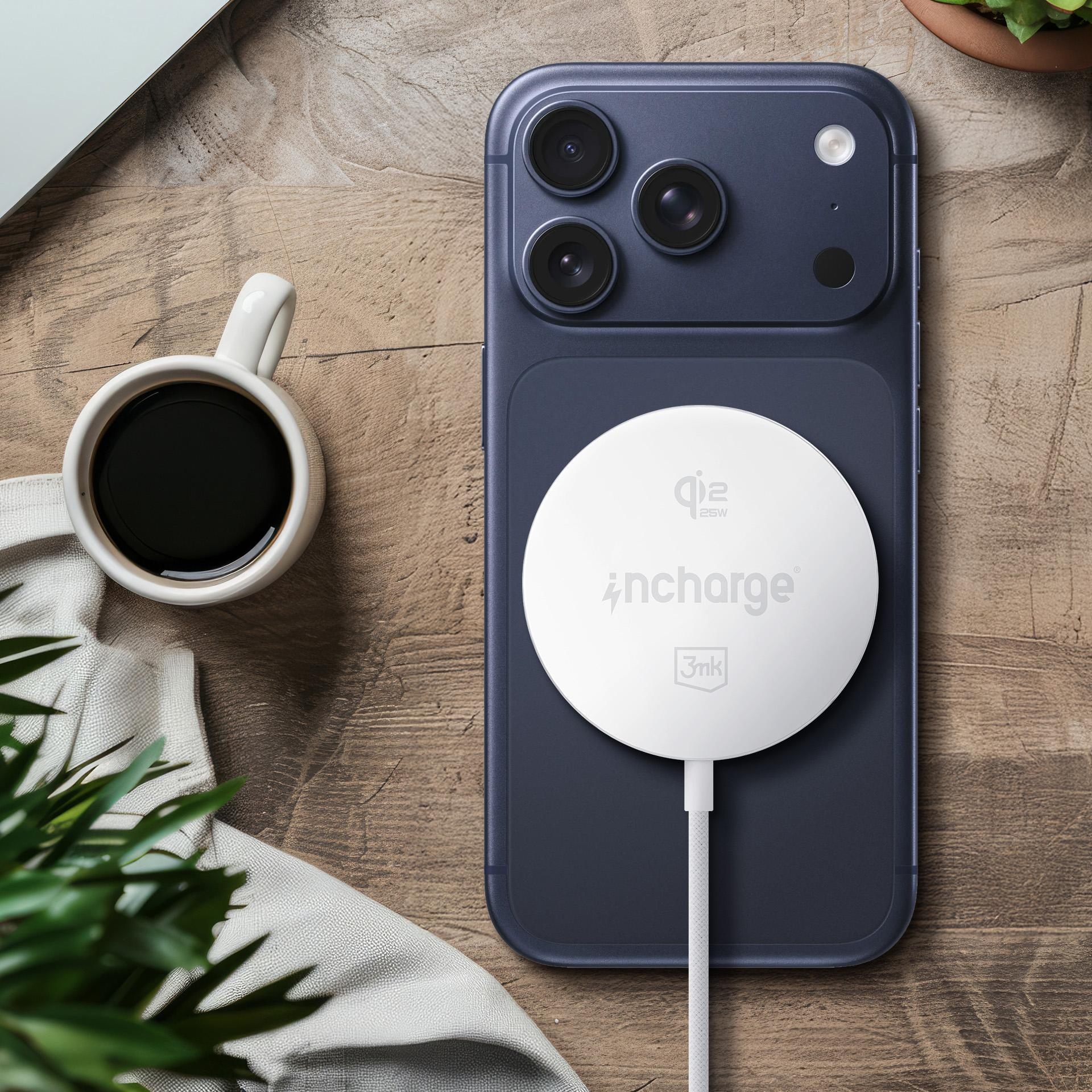 Czarny iPhone z białym okrągłym ładowarką bezprzewodową, obok białego kubka kawy na drewnianym stole.