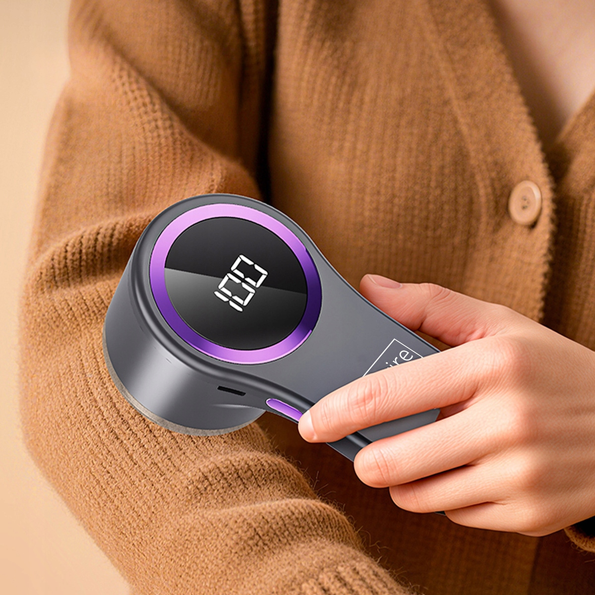 Golarka do tkanin z cyfrowym wyświetlaczem trzymana nad brązowym swetrem.