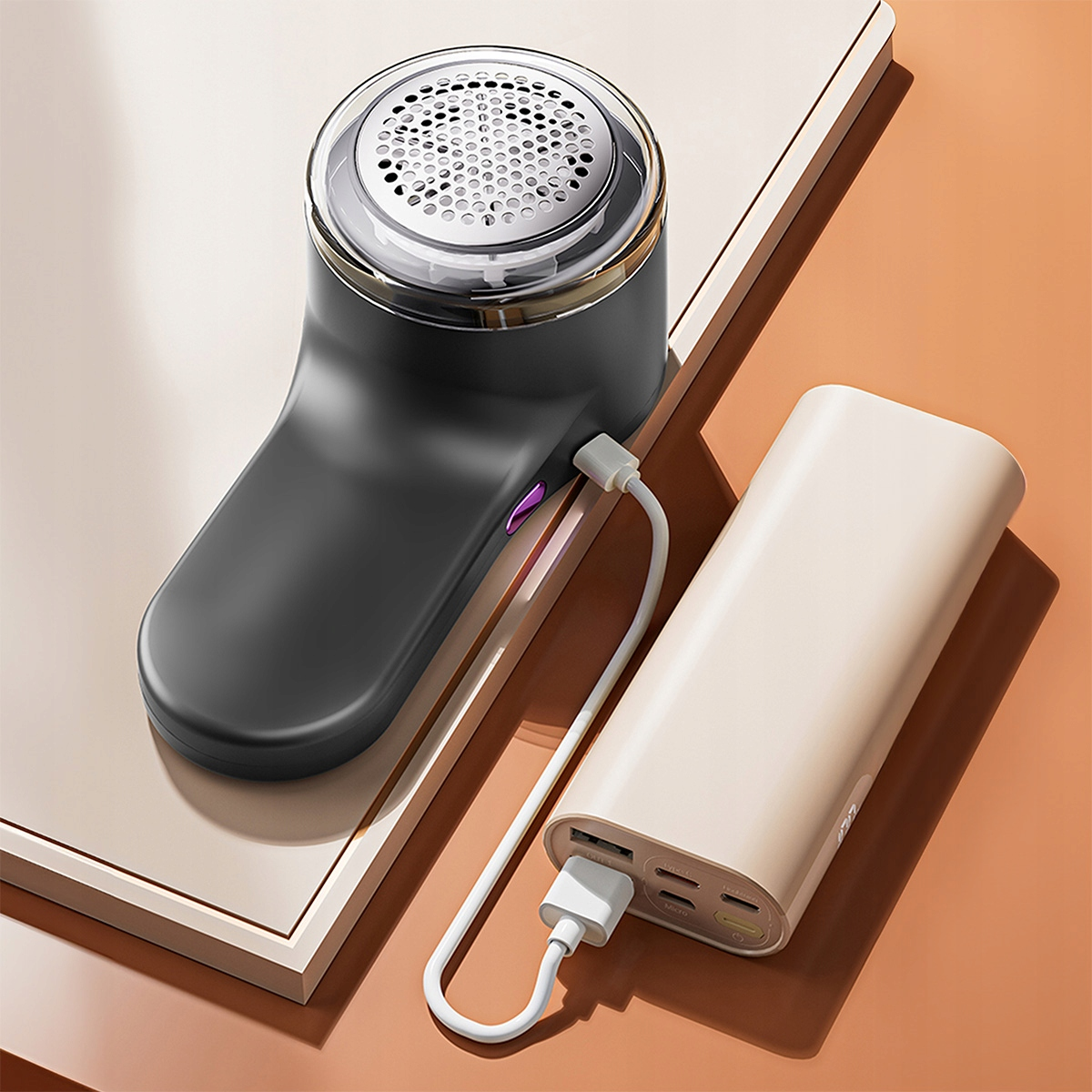 Czarna golarka do tkanin podłączona do kremowego powerbanku białym kablem.