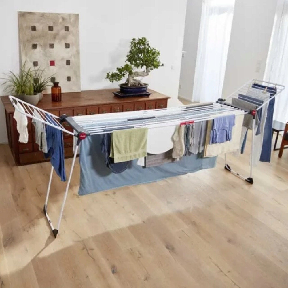 Stojak do suszenia prania z ubraniami stoi na drewnianej podłodze.