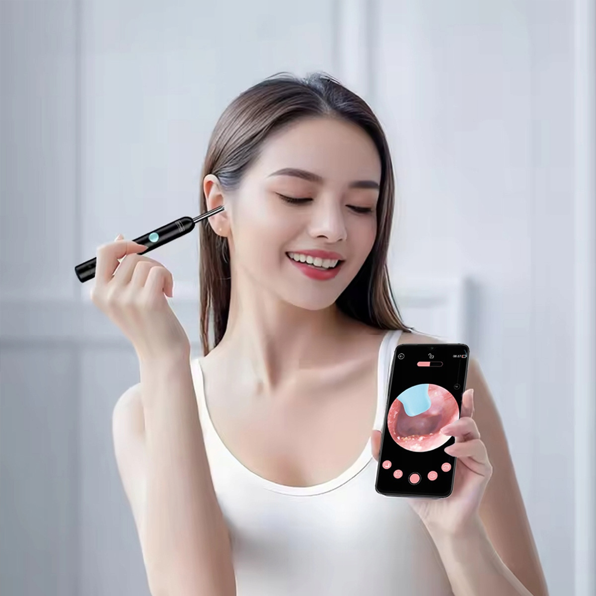 Kobieta używa urządzenia do czyszczenia uszu, trzyma telefon pokazujący widok kanału słuchowego.