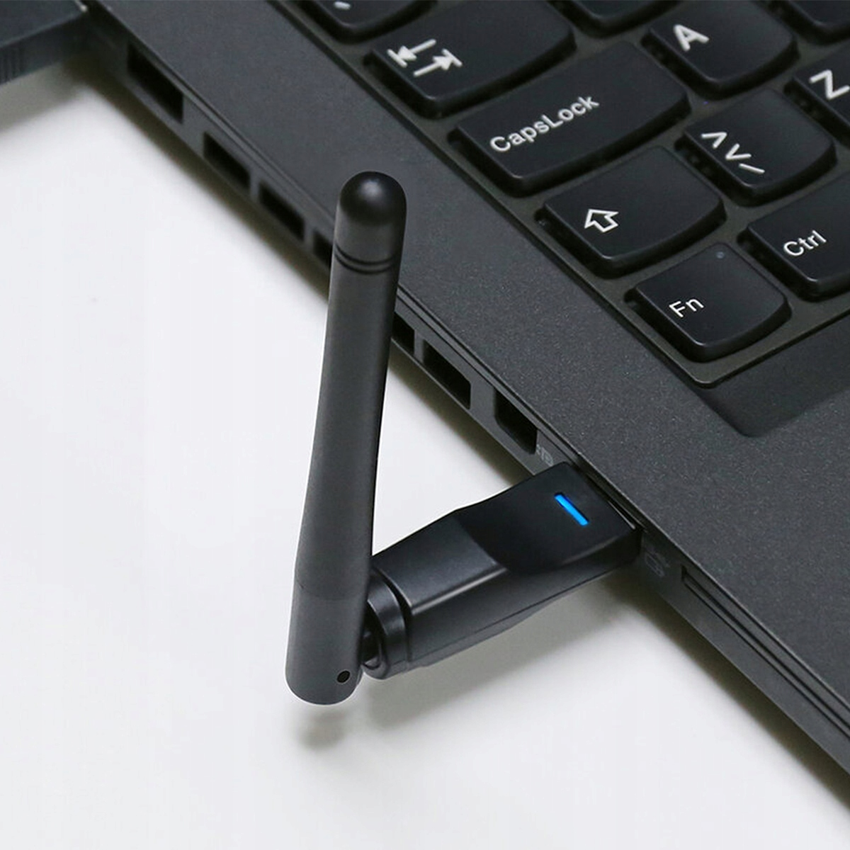 Czarna przejściówka WiFi USB z antenką jest podłączona do laptopa.