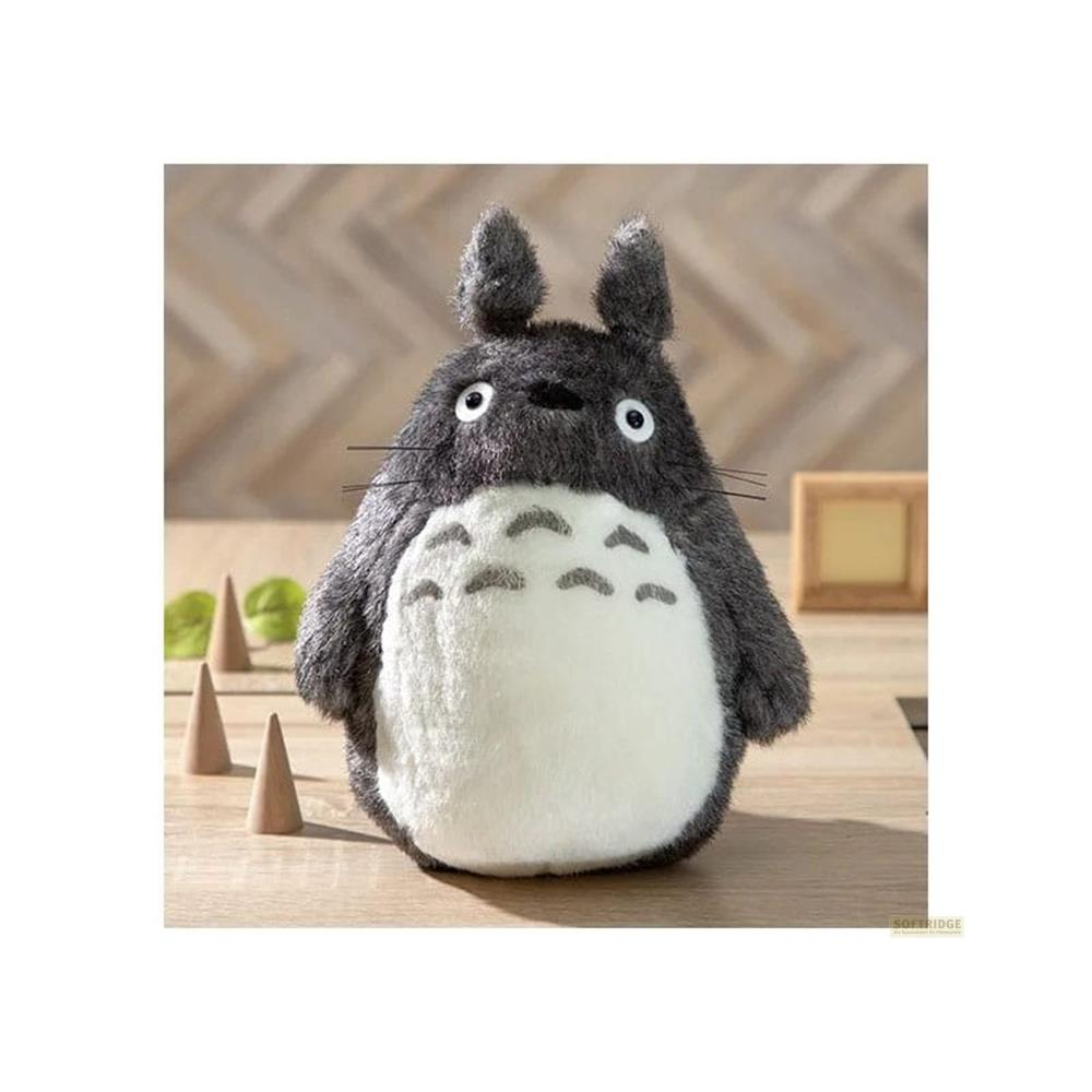 Un peluche Totoro grigio con pancia bianca seduto su un tavolo di legno.