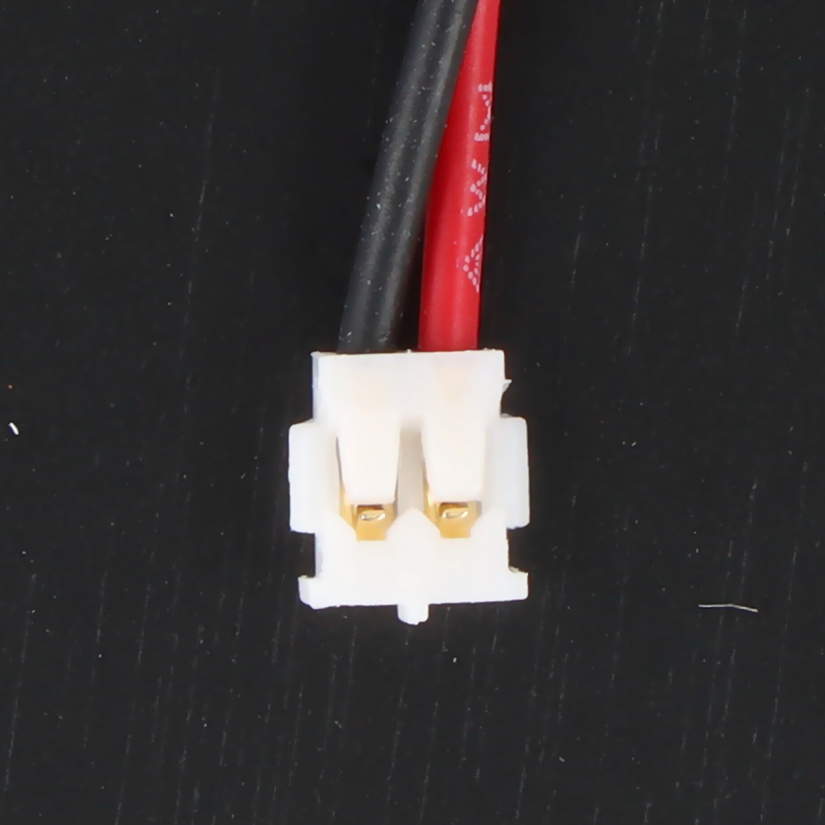 Un conector blanco con dos contactos dorados, unido a cables negro y rojo.
