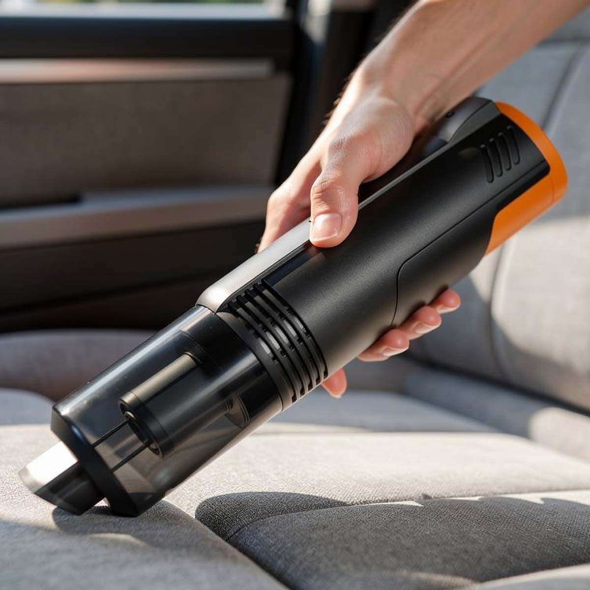 Mano tiene aspirapolvere portatile nero e arancione su sedili auto.