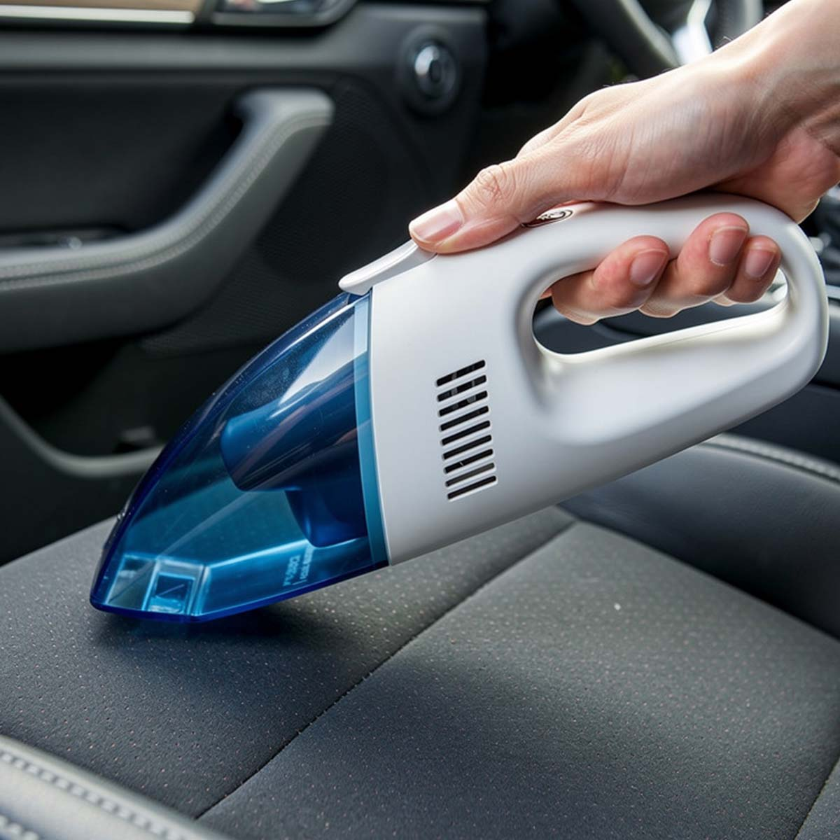 Mano tiene aspirapolvere bianco su sedile auto. Contenitore polvere blu.