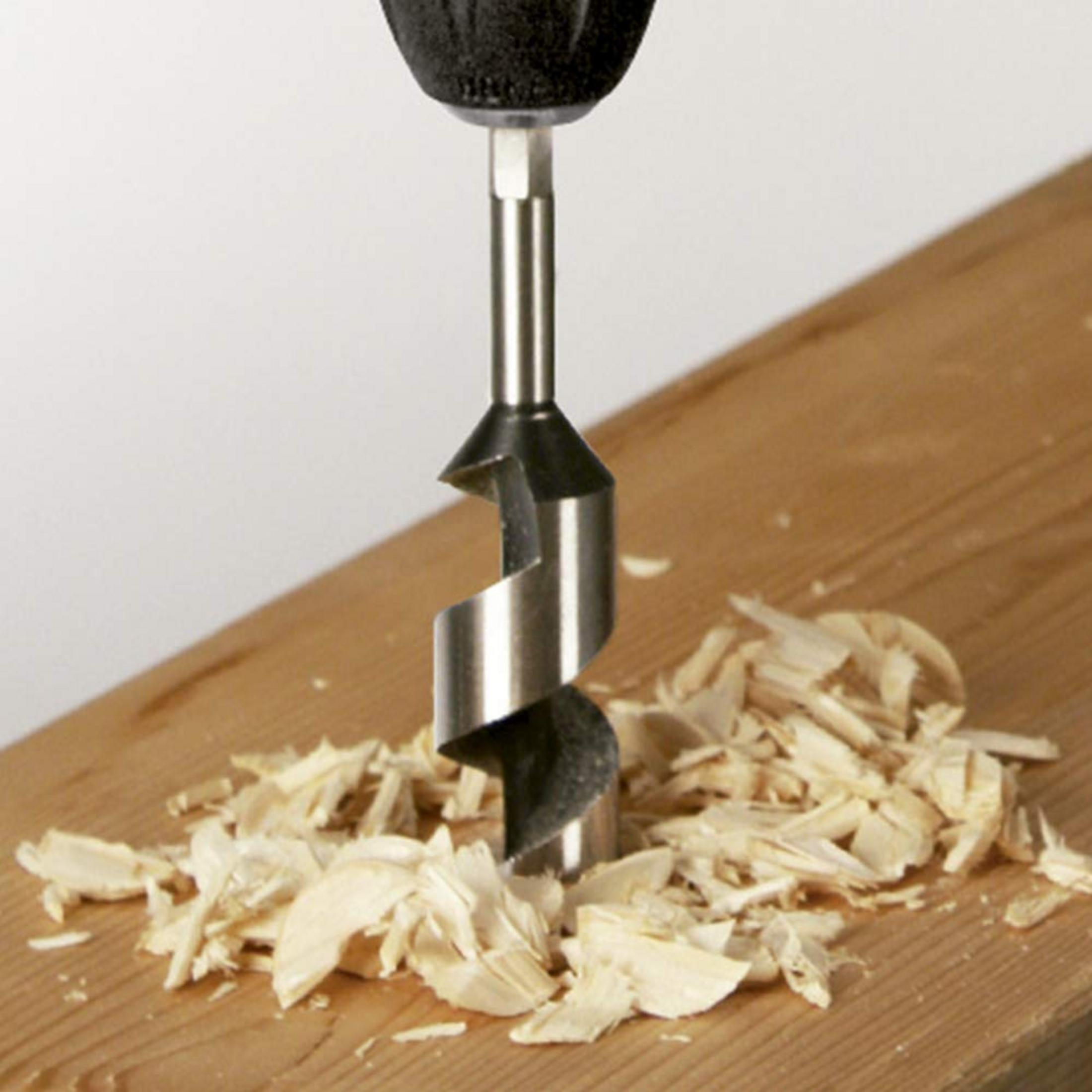 Wiertło wierci w drewnie, wokół leżą wióry drzewne.