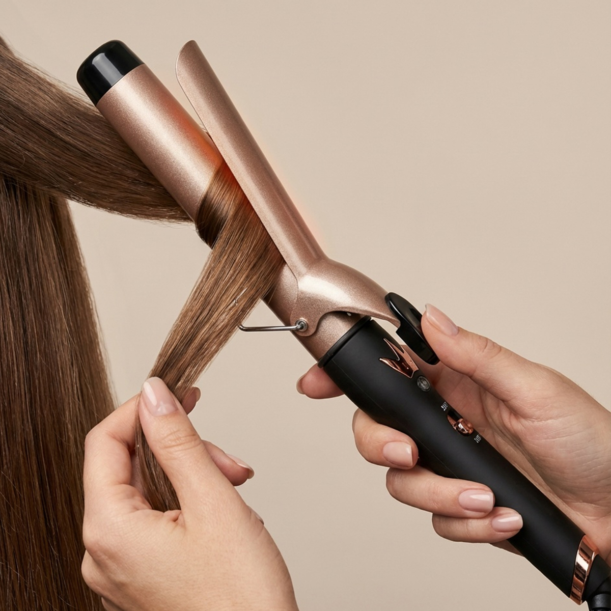 Una mano usa un rizador para peinar cabello castaño.