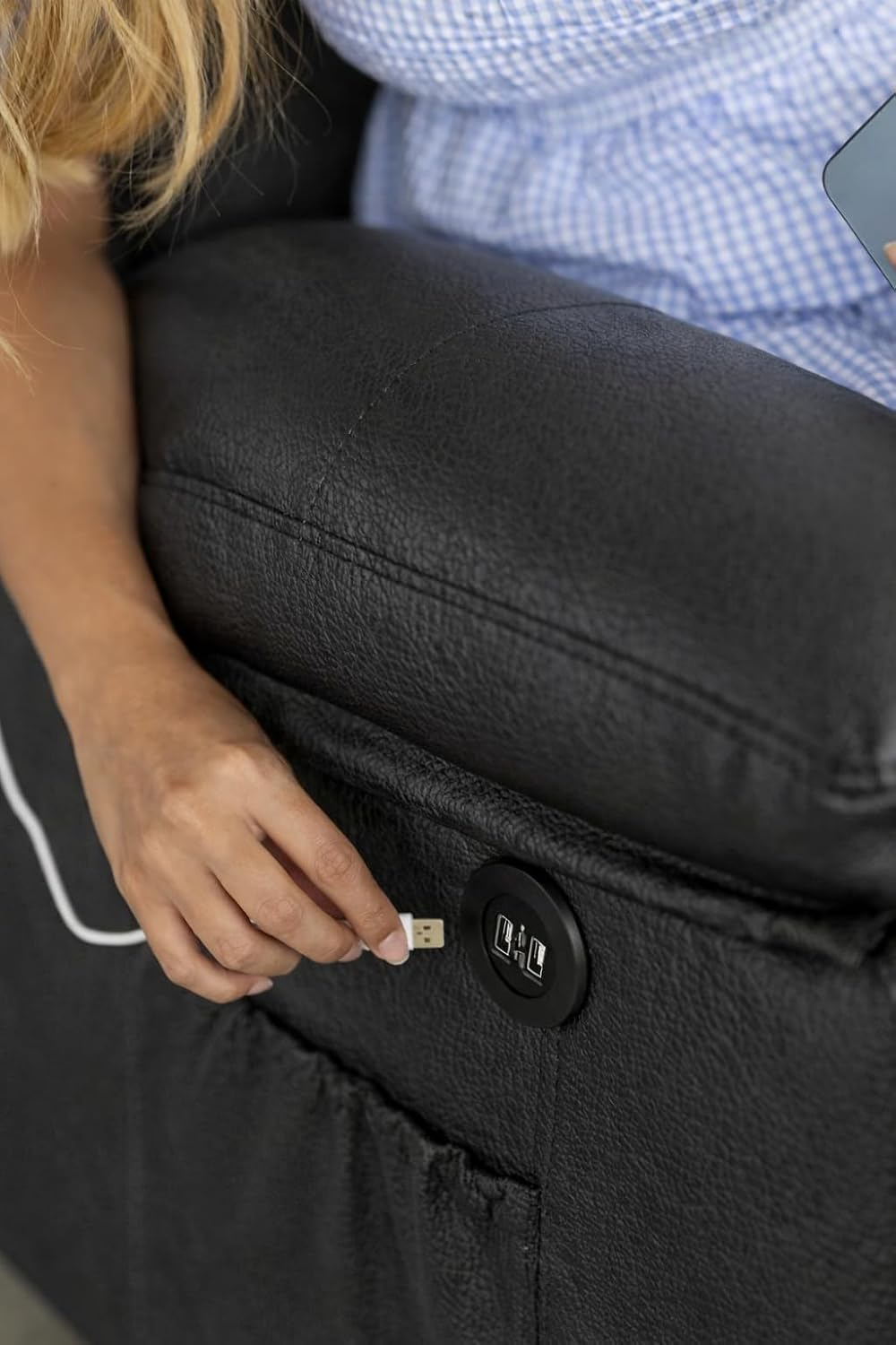 Una mano inserta un cable USB en un puerto de carga en un sofá de cuero negro.