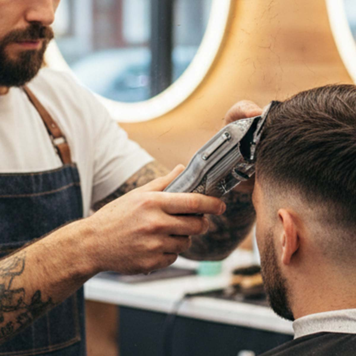 Un barbero recorta el pelo de un hombre con una cortapelos eléctrica.