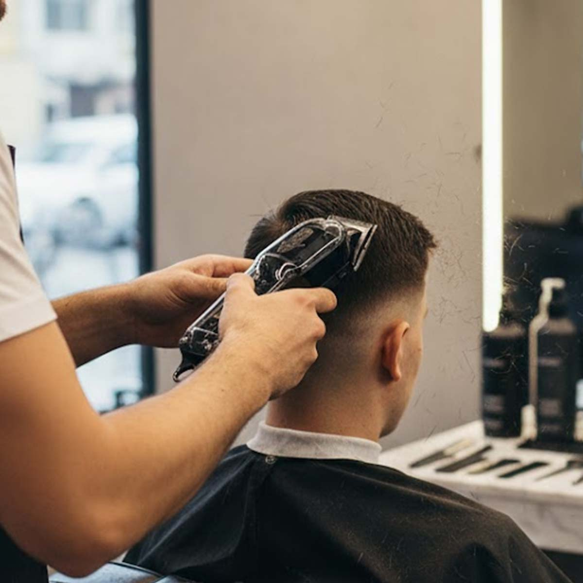 Un barbero corta el pelo de un hombre con una cortapelos eléctrica. Se ven restos de pelo.