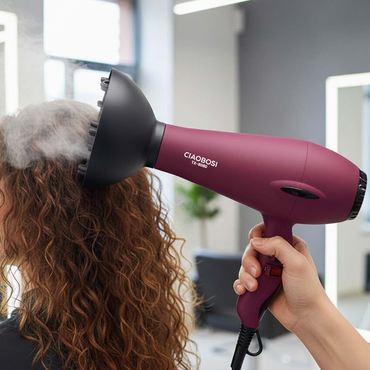 Eine Hand hält einen bordeauxroten Haartrockner mit Diffusor an lockigem Haar.