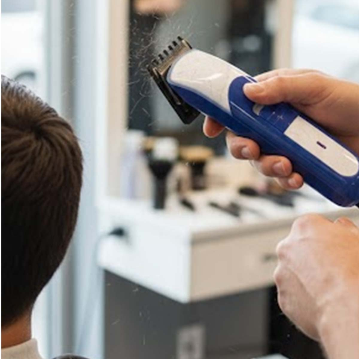 Un coiffeur coupe les cheveux d'un client avec une tondeuse bleue et blanche.