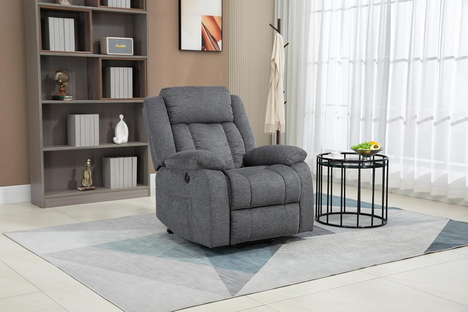 Un sillón reclinable gris sobre una alfombra, junto a una mesa con fruta.