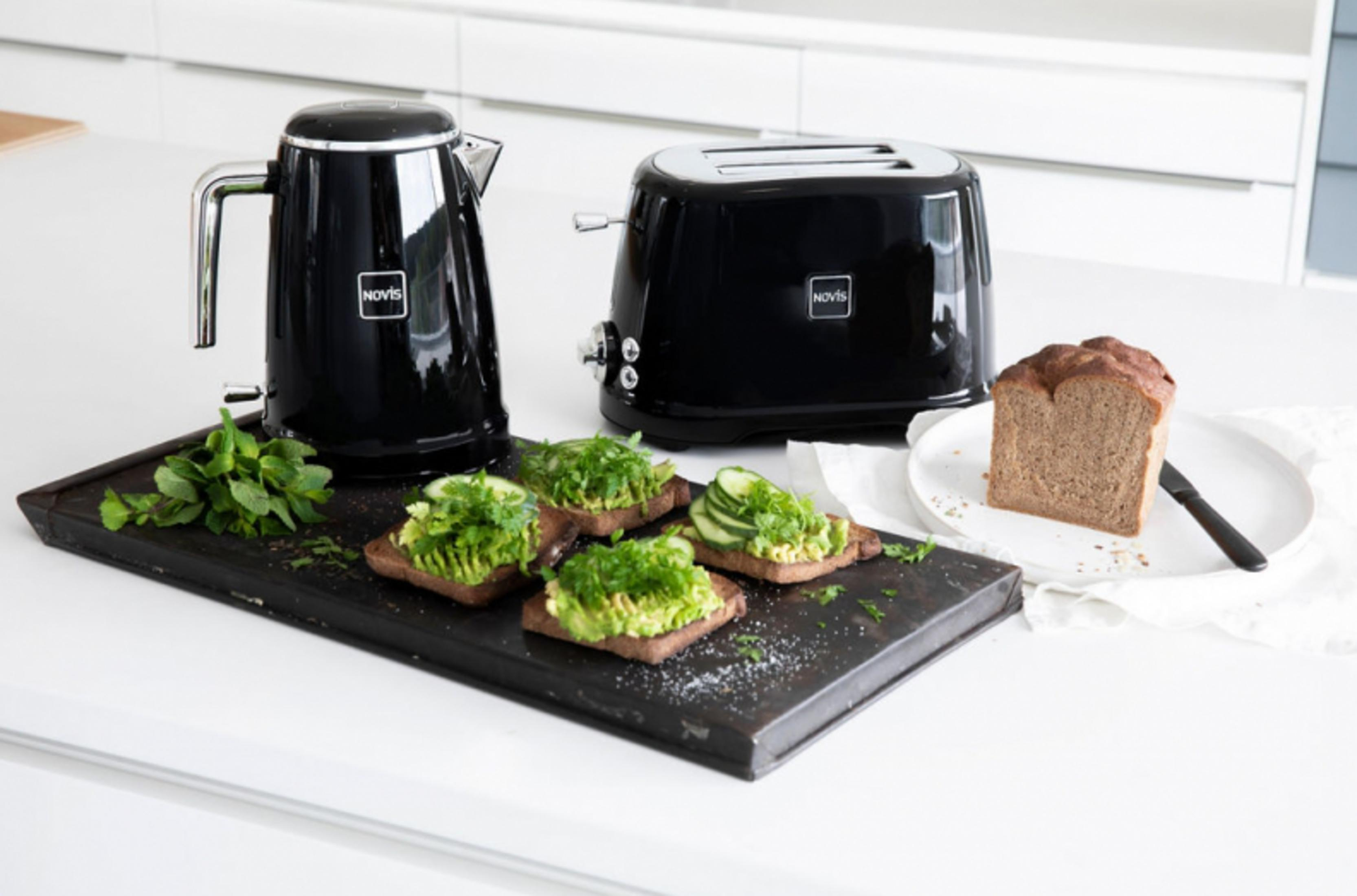 Schwarzer Wasserkocher, Toaster, Avocado-Toast und Brot auf einem Tisch.