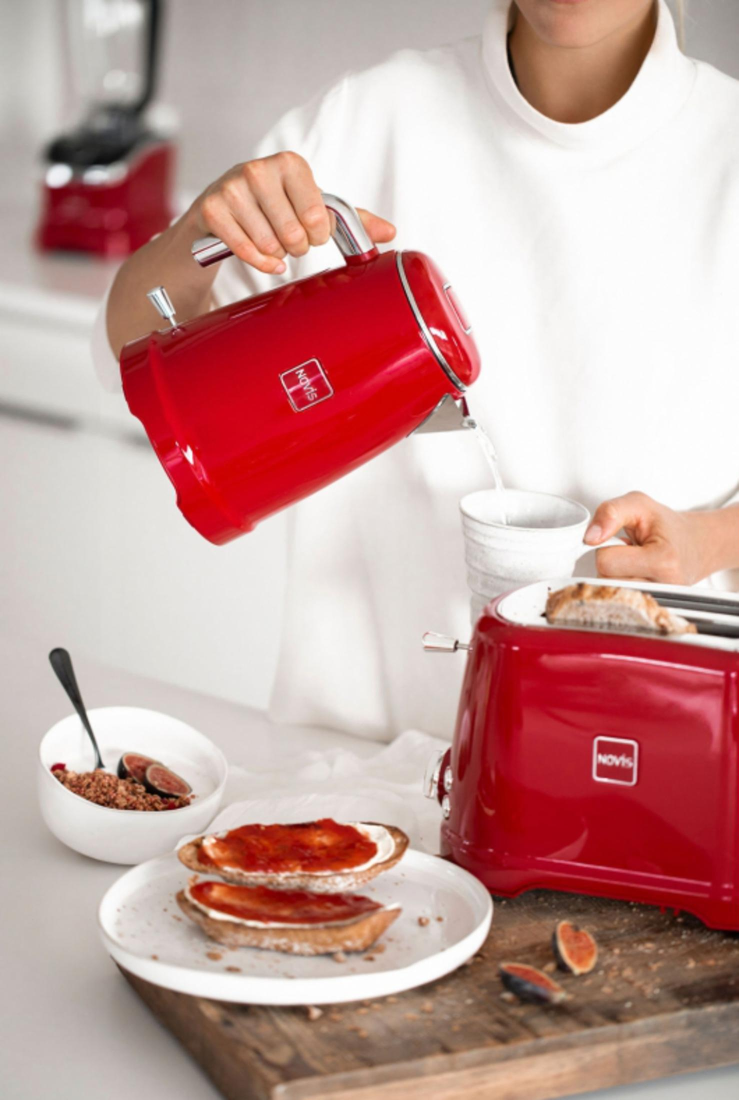 Eine rote Novis-Kaffeemaschine gießt Wasser in eine Tasse über Toast.