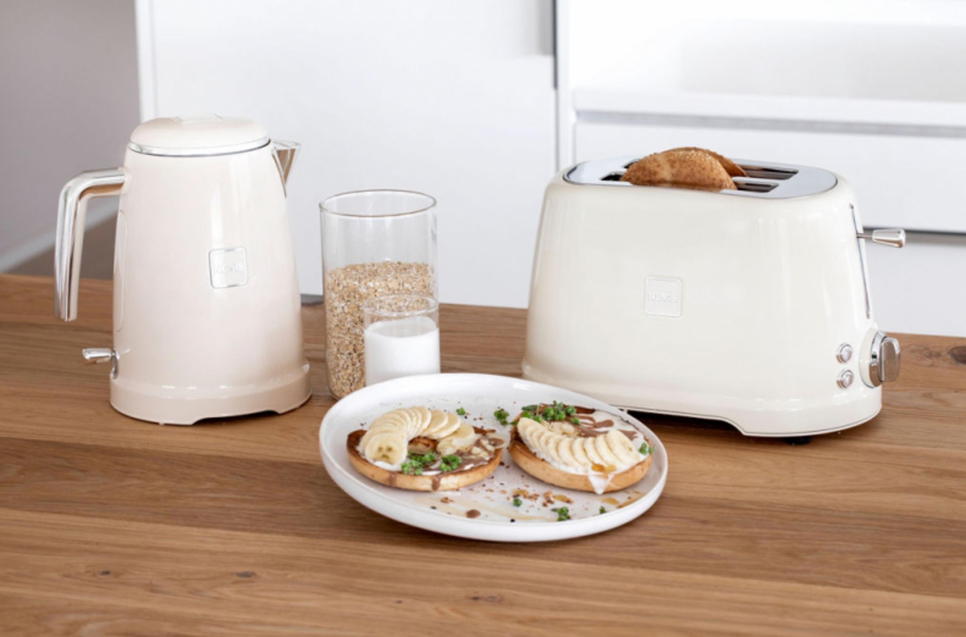 Ein cremefarbener Toaster mit Brot, ein Wasserkocher, ein Glas Müsli und Milch daneben.