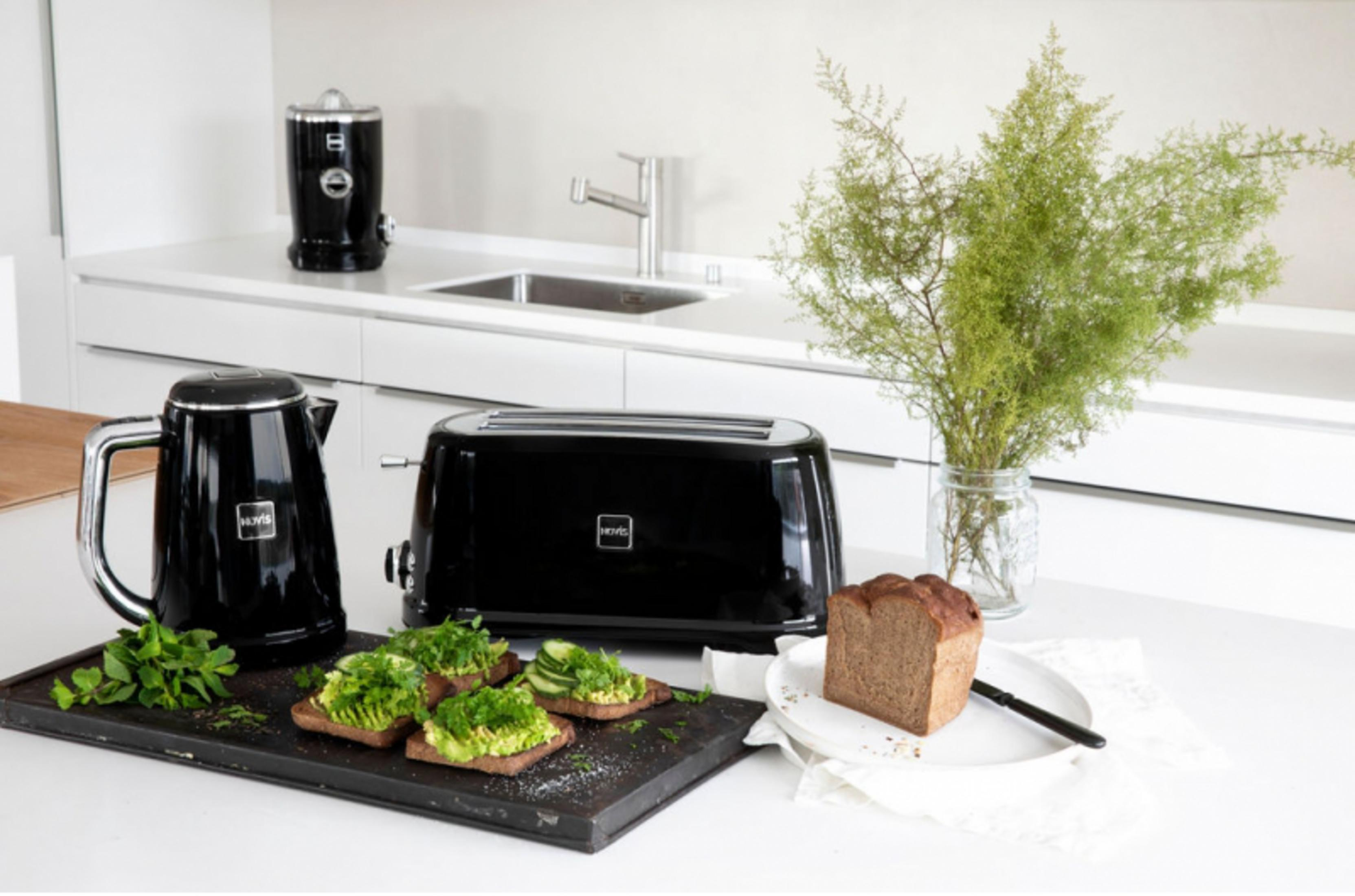 Schwarzer Wasserkocher, Toaster, Brot und Avocado-Toast auf einer weißen Arbeitsplatte.