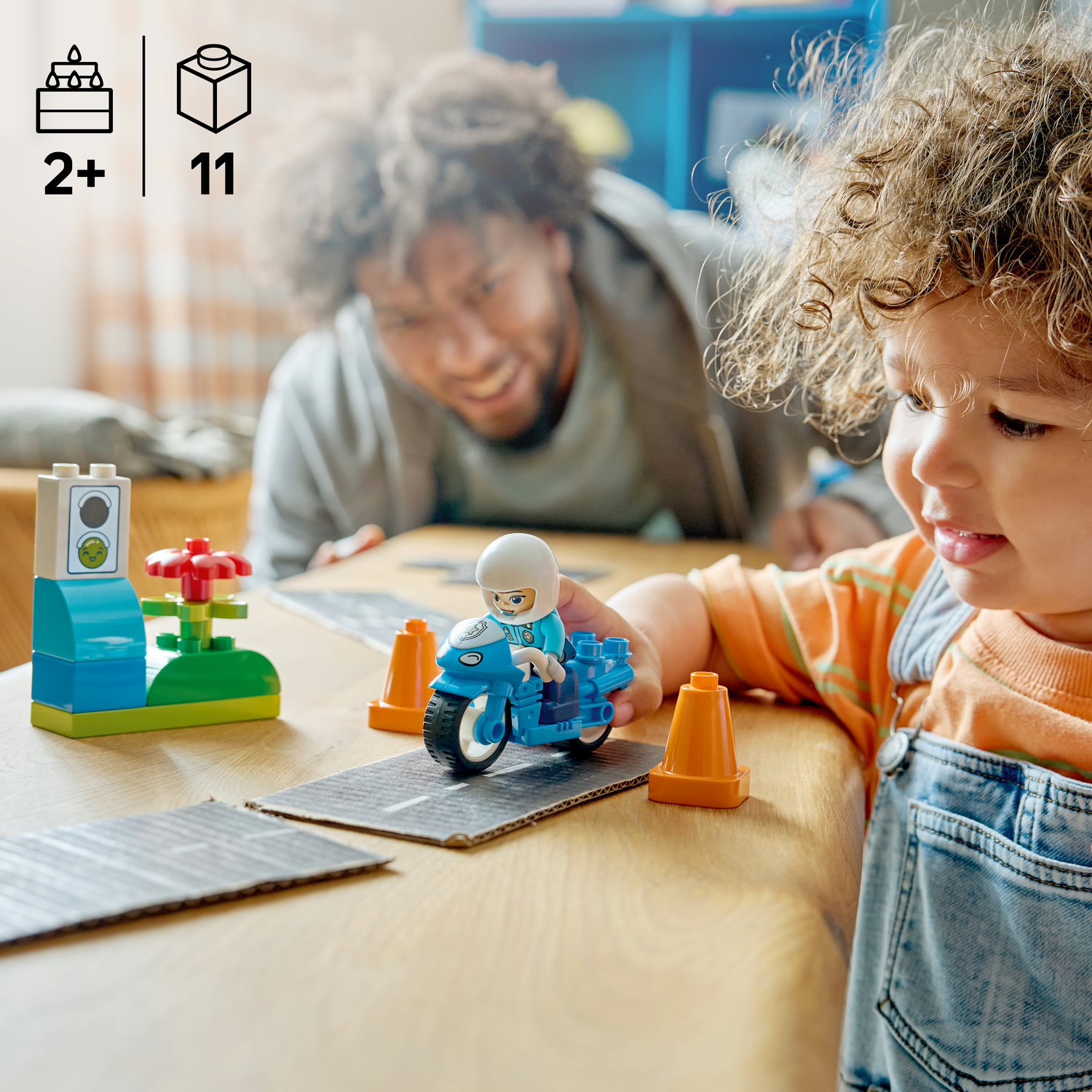 Baba ve çocuk ahşap masada Duplo oyuncaklarıyla oynuyor.