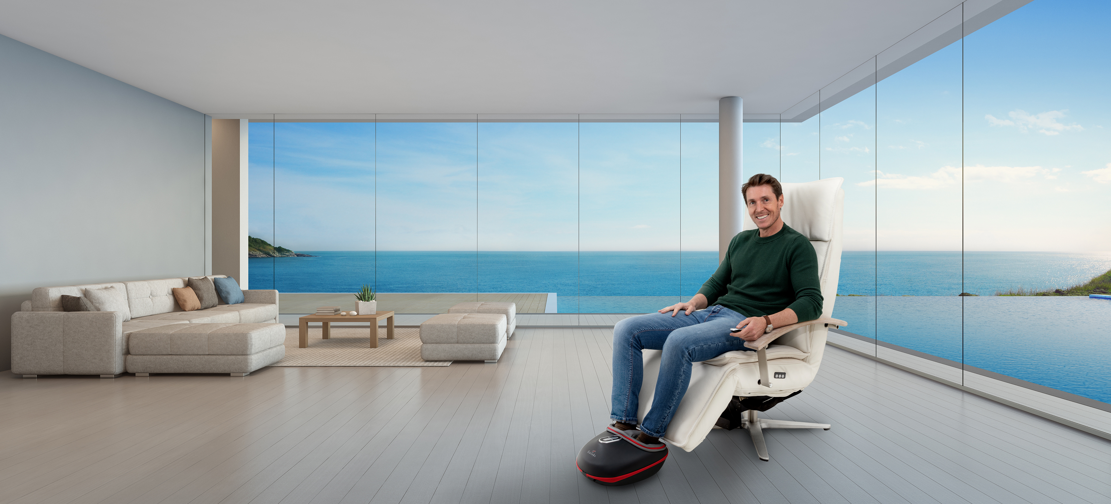 Mężczyzna w fotelu nad morzem, z masażerem do stóp i pilotem.