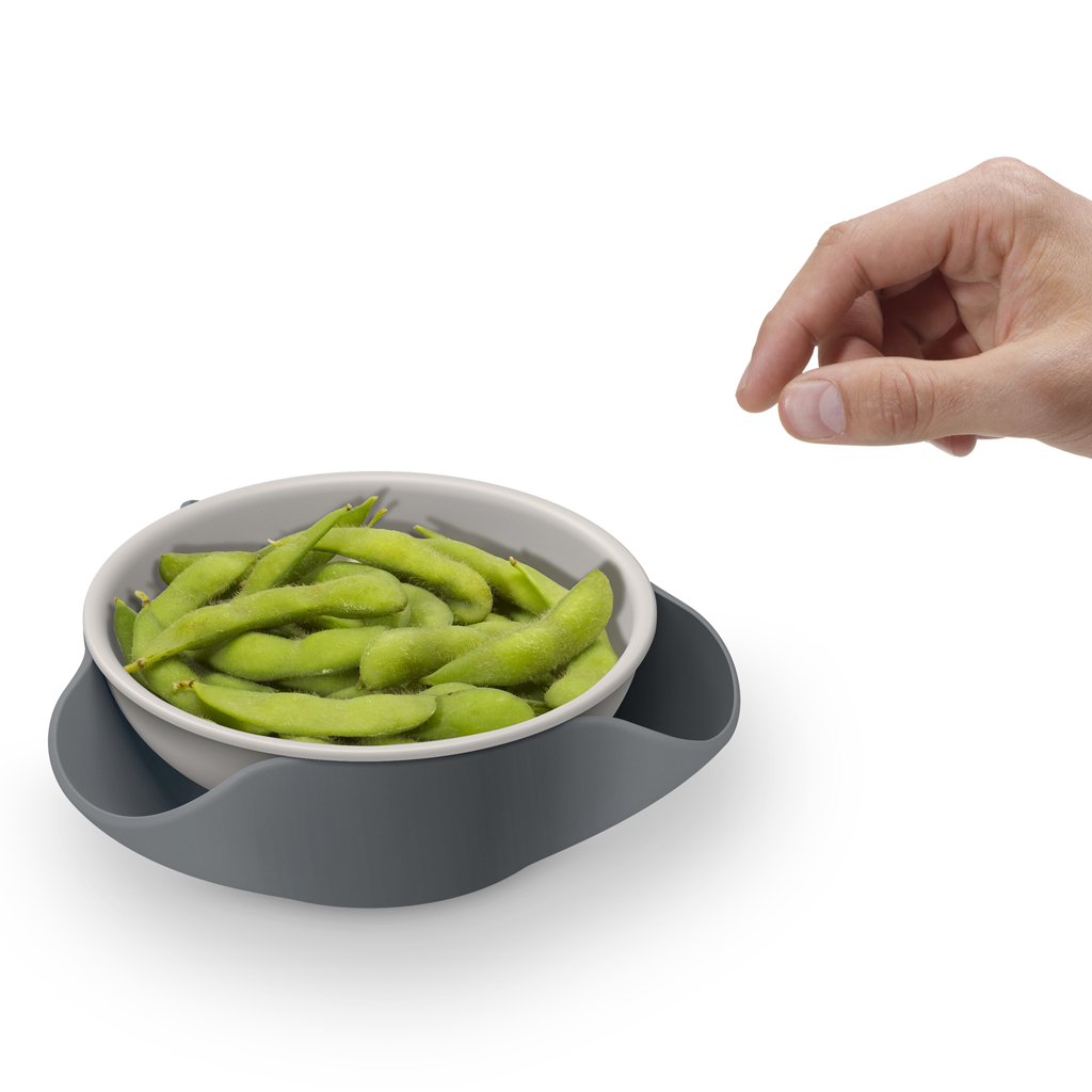 Una mano afferra una ciotola di edamame su un vassoio grigio.