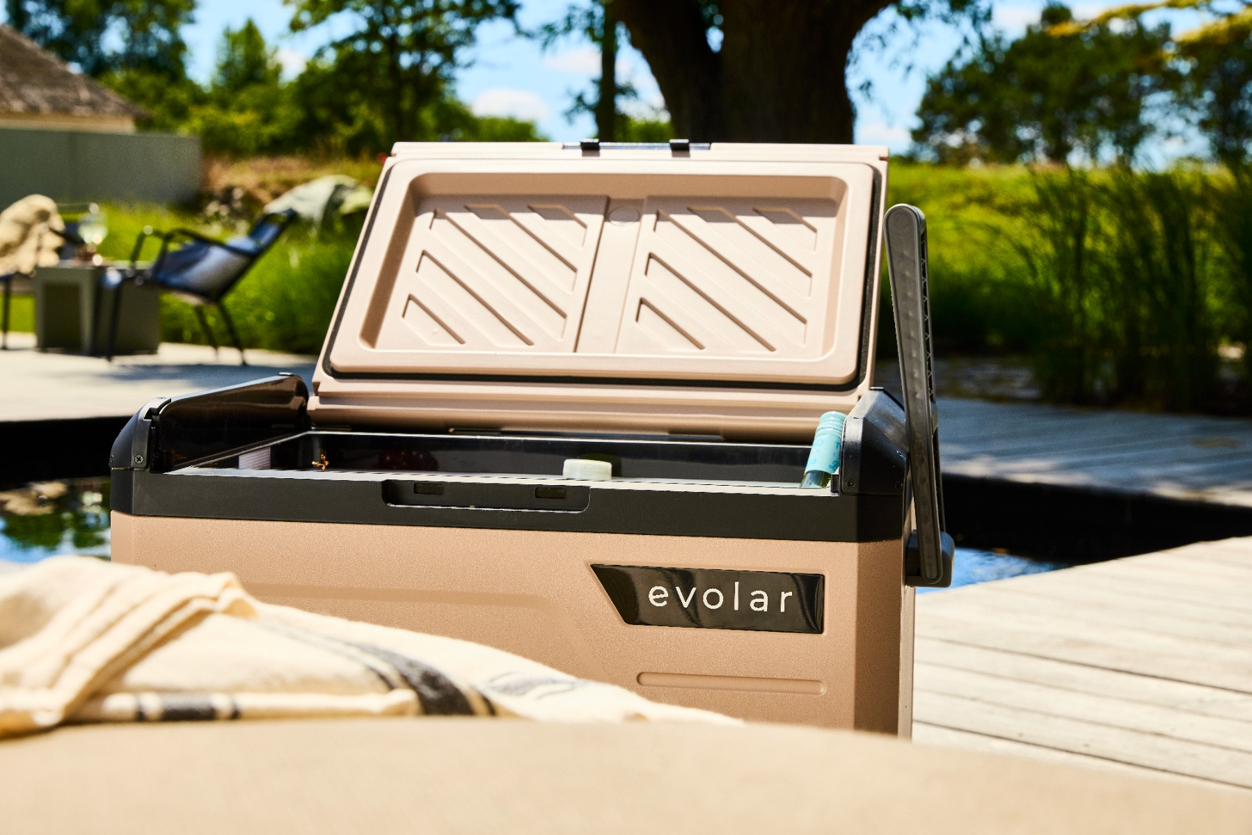 Una borsa frigo aperta color beige si trova su un ponte di legno vicino a una piscina.