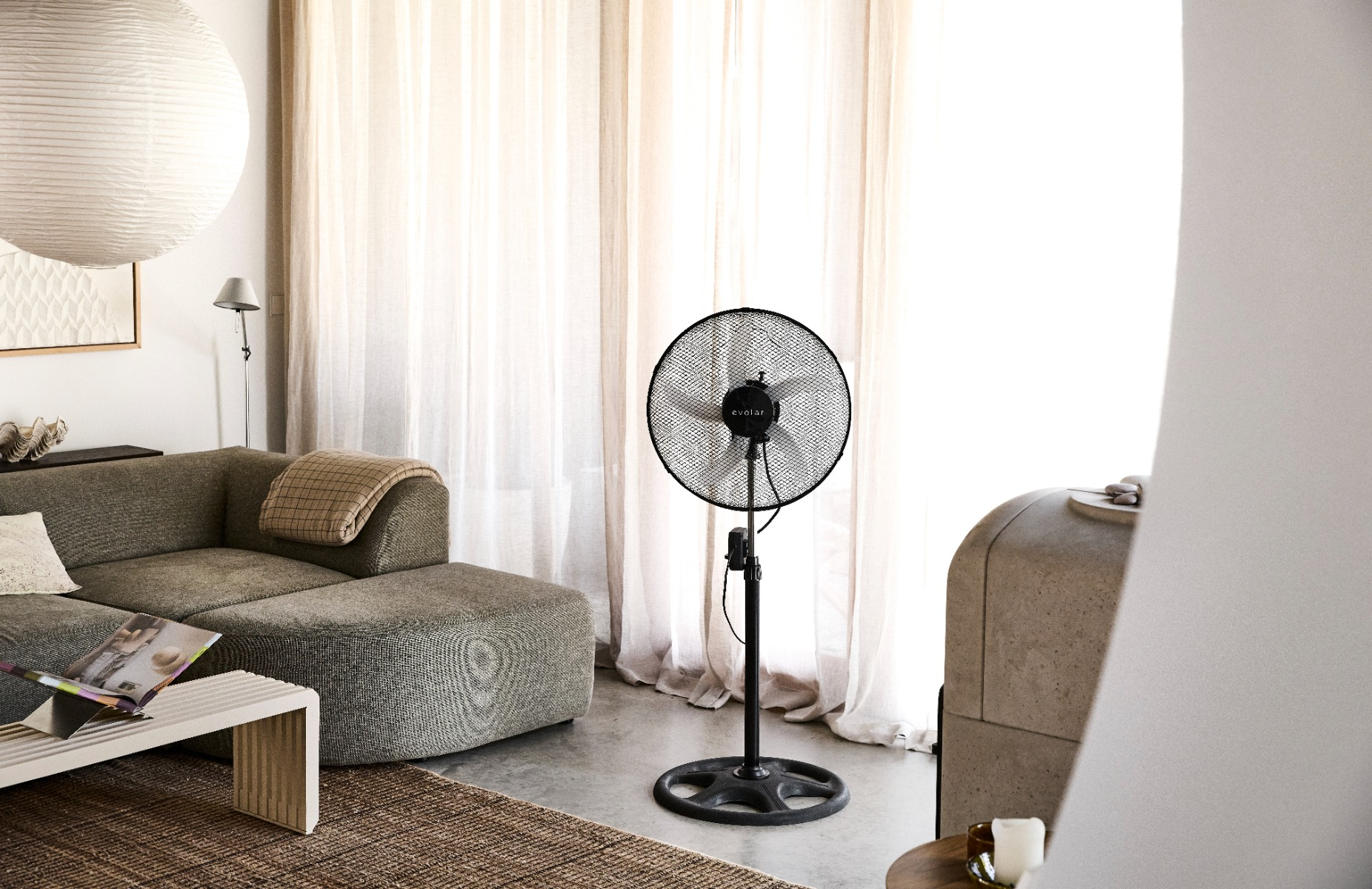 A black standing fan is next to a gray sofa with a blanket.