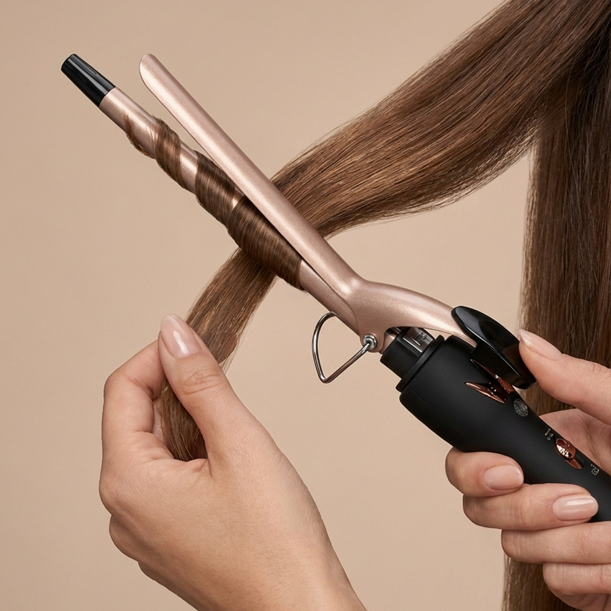 Eine Hand kräuselt braunes Haar mit einem Lockenstab.