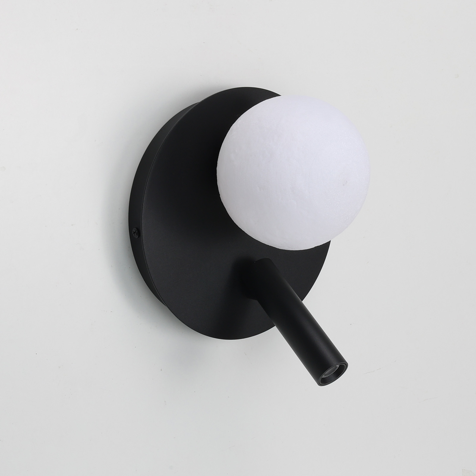 Una moderna lámpara de pared negra con base redonda y orbe de cristal.