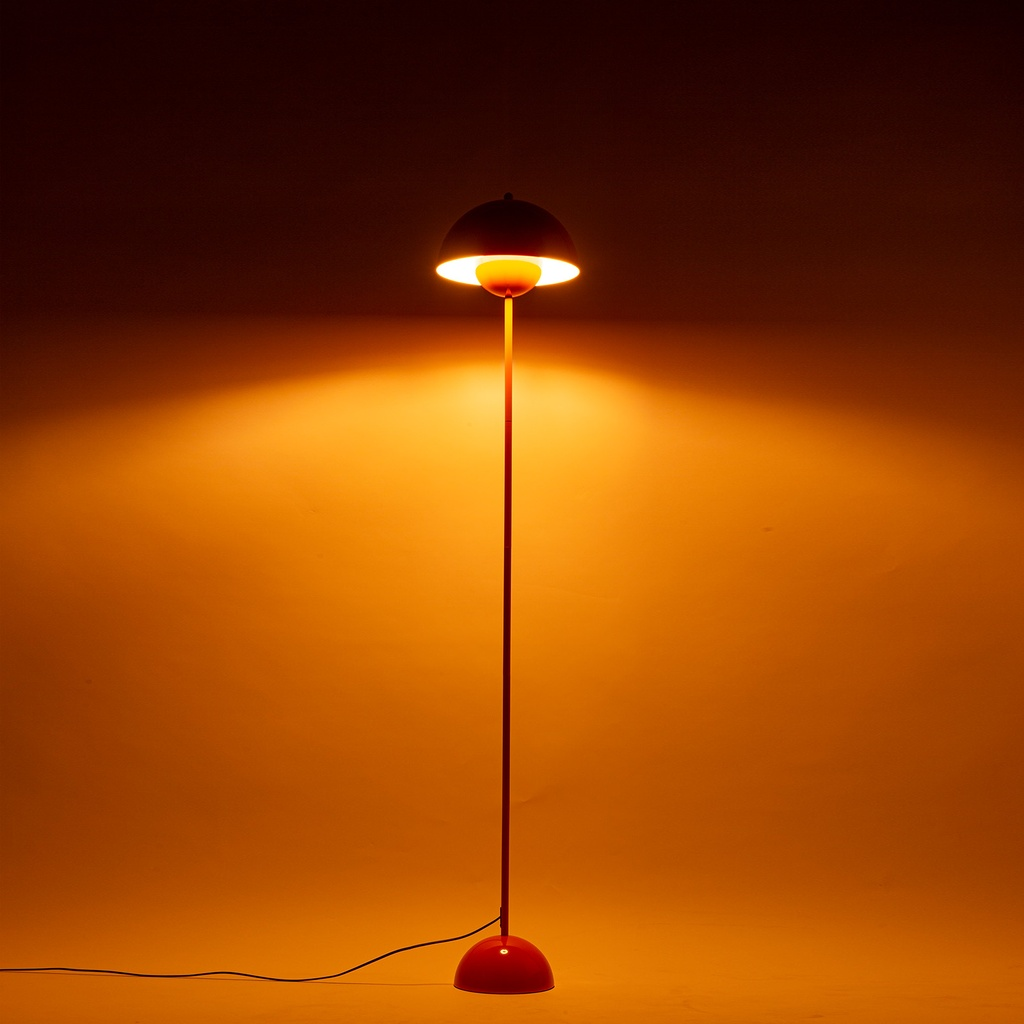 Una lámpara de pie roja con pantalla y base redondas ilumina una pared naranja.