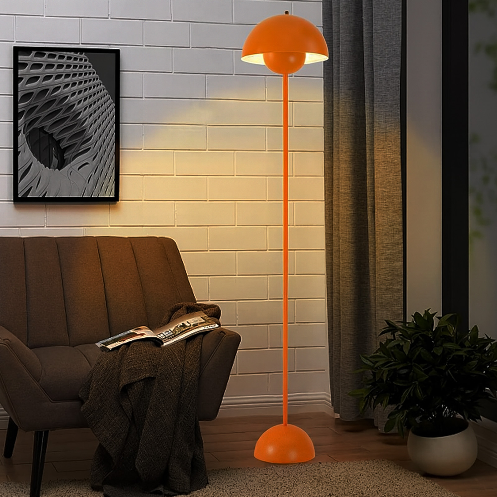 Una lámpara de pie naranja con pantalla de cúpula junto a un sillón marrón con manta y libro.
