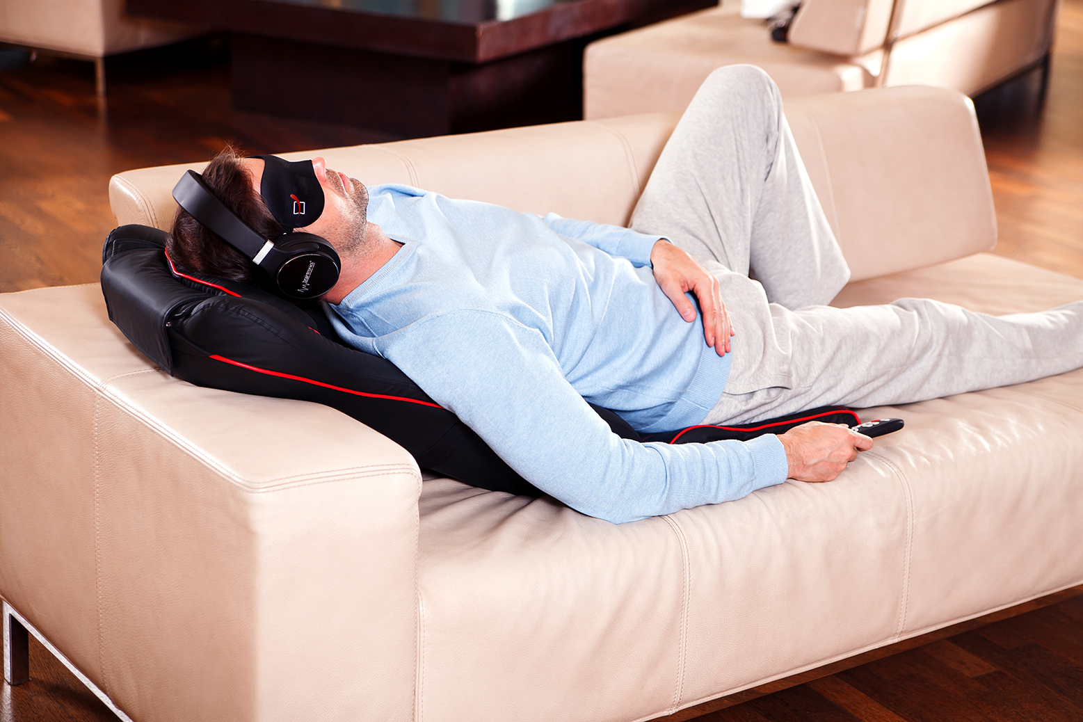 Mężczyzna w masce na oczy i słuchawkach leży na kanapie z pilotem.