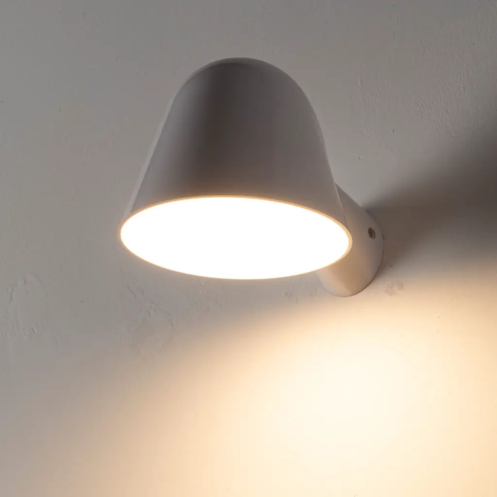 Una lámpara de pared blanca con pantalla hacia abajo está iluminada.