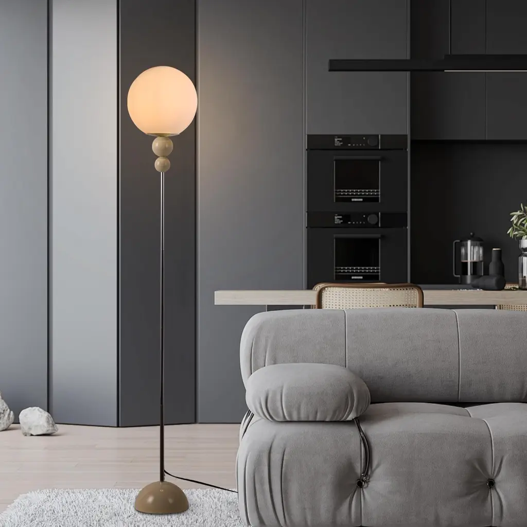 Un espacio de vida moderno con sofá, lámpara de pie y zona de cocina oscura.