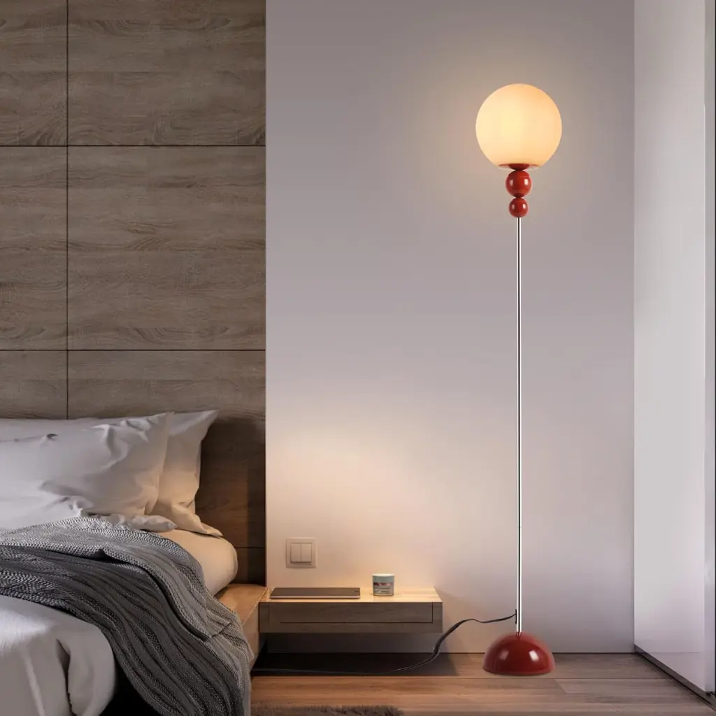 Una lámpara de pie roja con pantalla esférica junto a una cama con pared de madera.