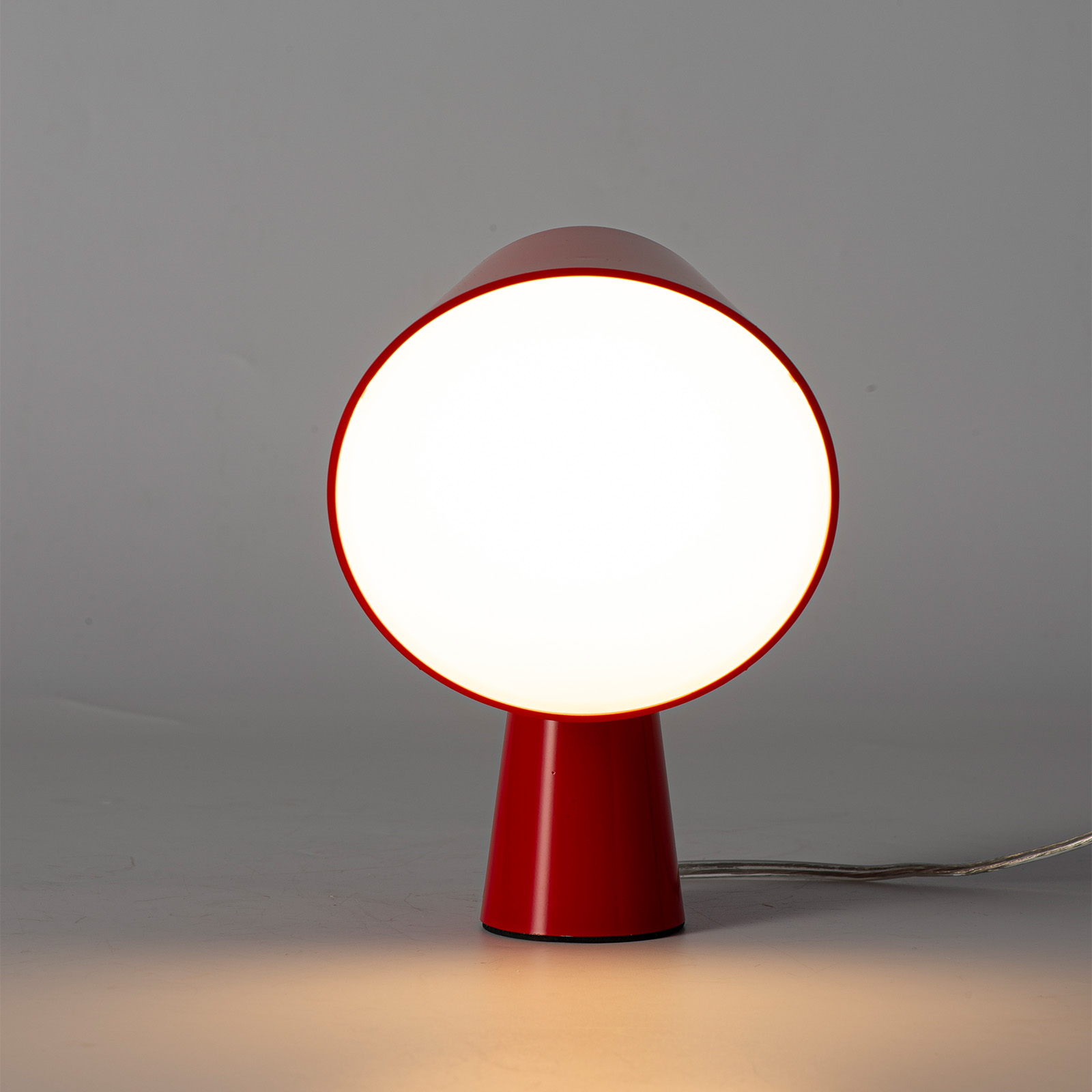 Una lámpara roja con pantalla redonda y brillante sobre fondo gris.
