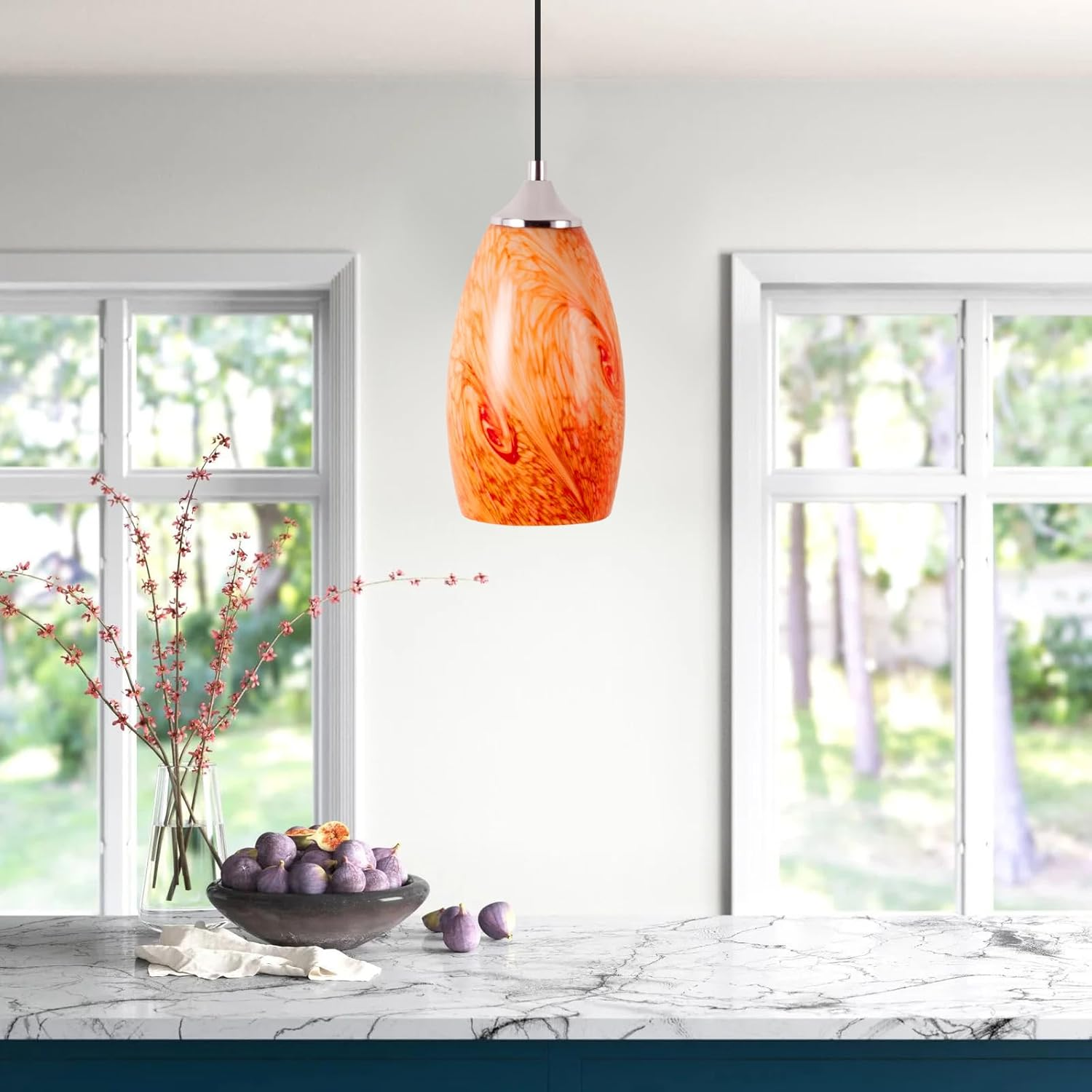 Lámpara colgante naranja y blanca sobre encimera de mármol con fruta y flores.