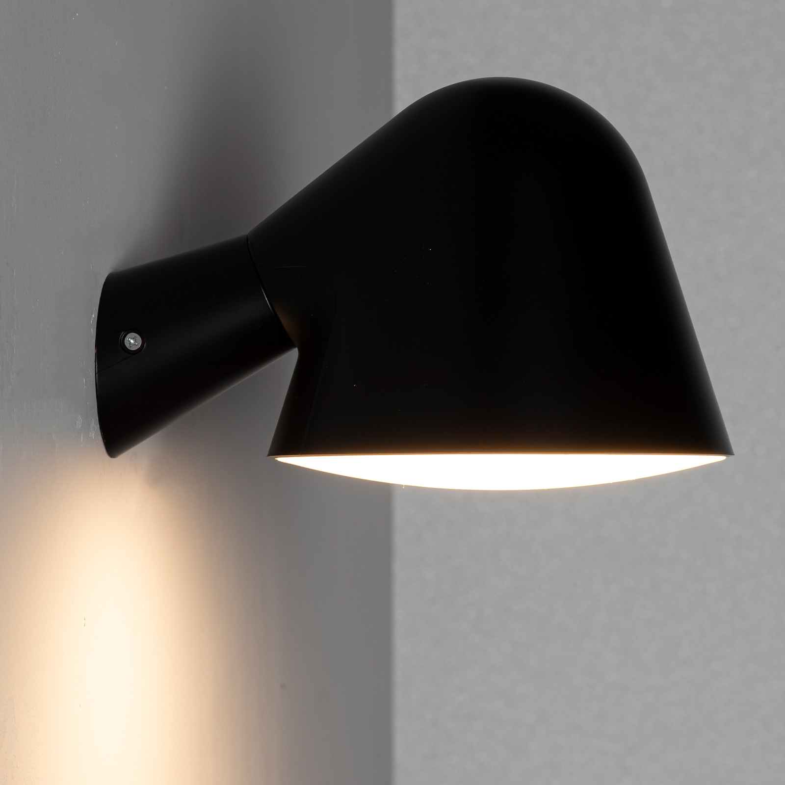 Una lámpara de pared negra con pantalla cónica ilumina hacia abajo.
