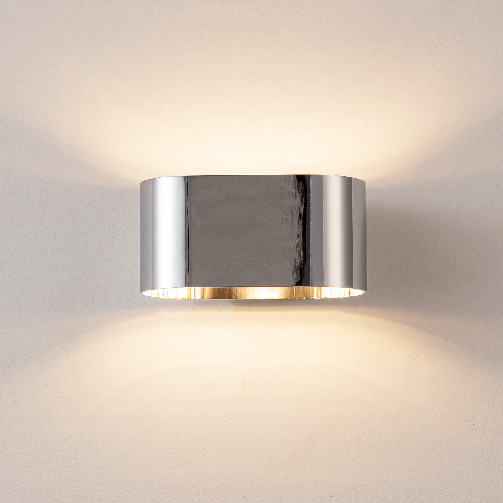 Una lámpara de pared cilíndrica cromada y brillante ilumina la pared.