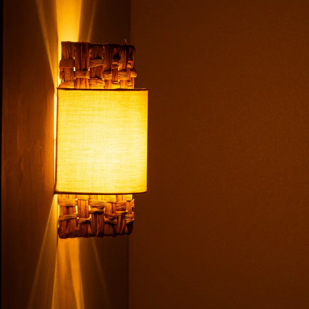 Una lámpara de pared con cuerpo tejido y pantalla de tela amarilla emite luz cálida.