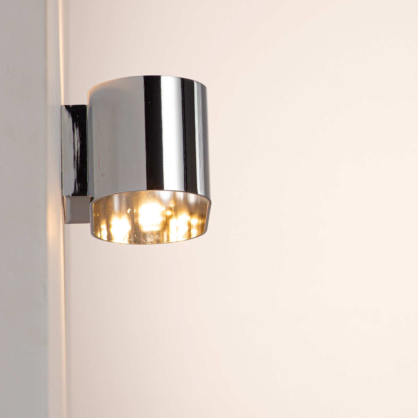 Una lámpara de pared cilíndrica y brillante con una sección inferior transparente que emite luz.