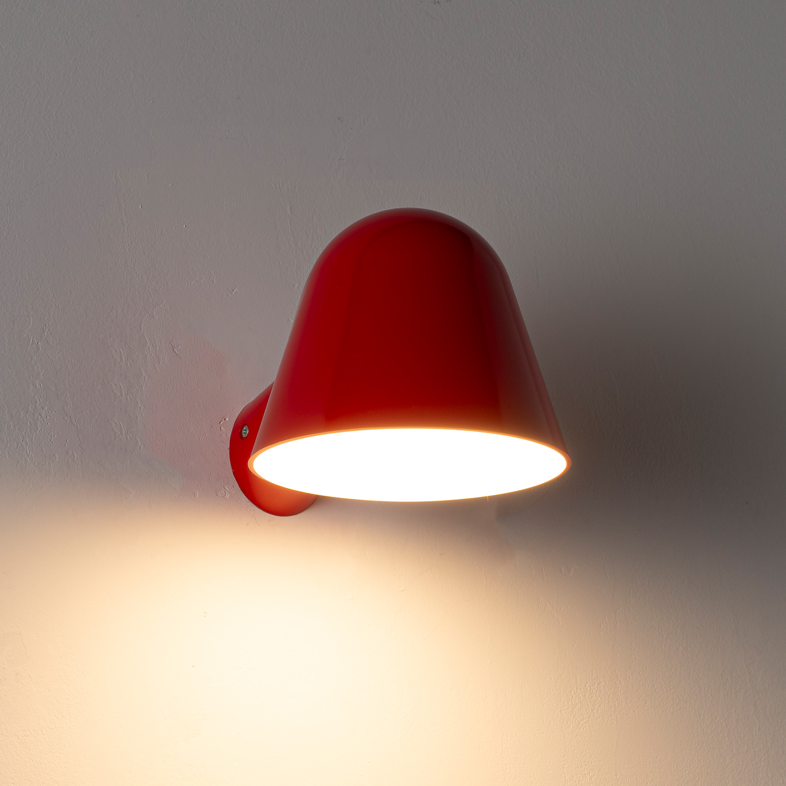Una lámpara de pared roja brilla intensamente en una pared gris texturizada.