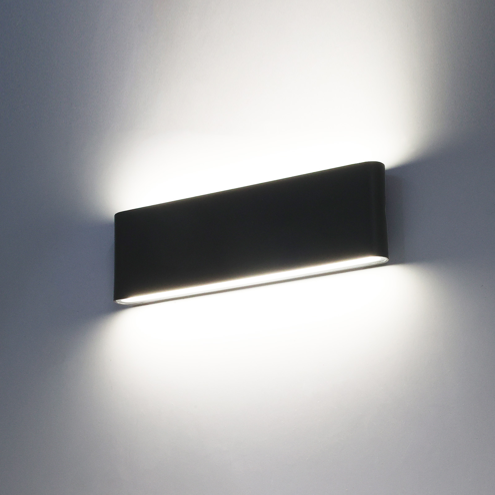 Un aplique de pared negro emite luz blanco cálido hacia arriba y abajo.