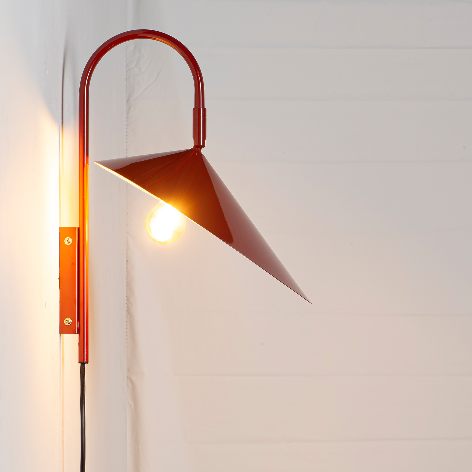 Una lámpara de pared roja con brazo curvo y pantalla cónica.