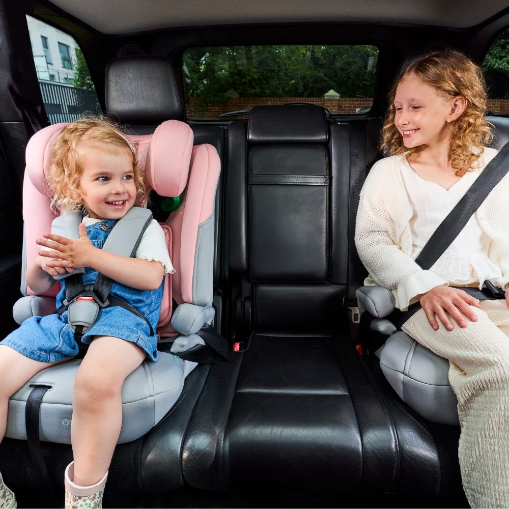 Zwei Mädchen sitzen in einem Auto auf Kindersitzen. Ein Kleinkind in Pink, ein älteres Kind in Creme.
