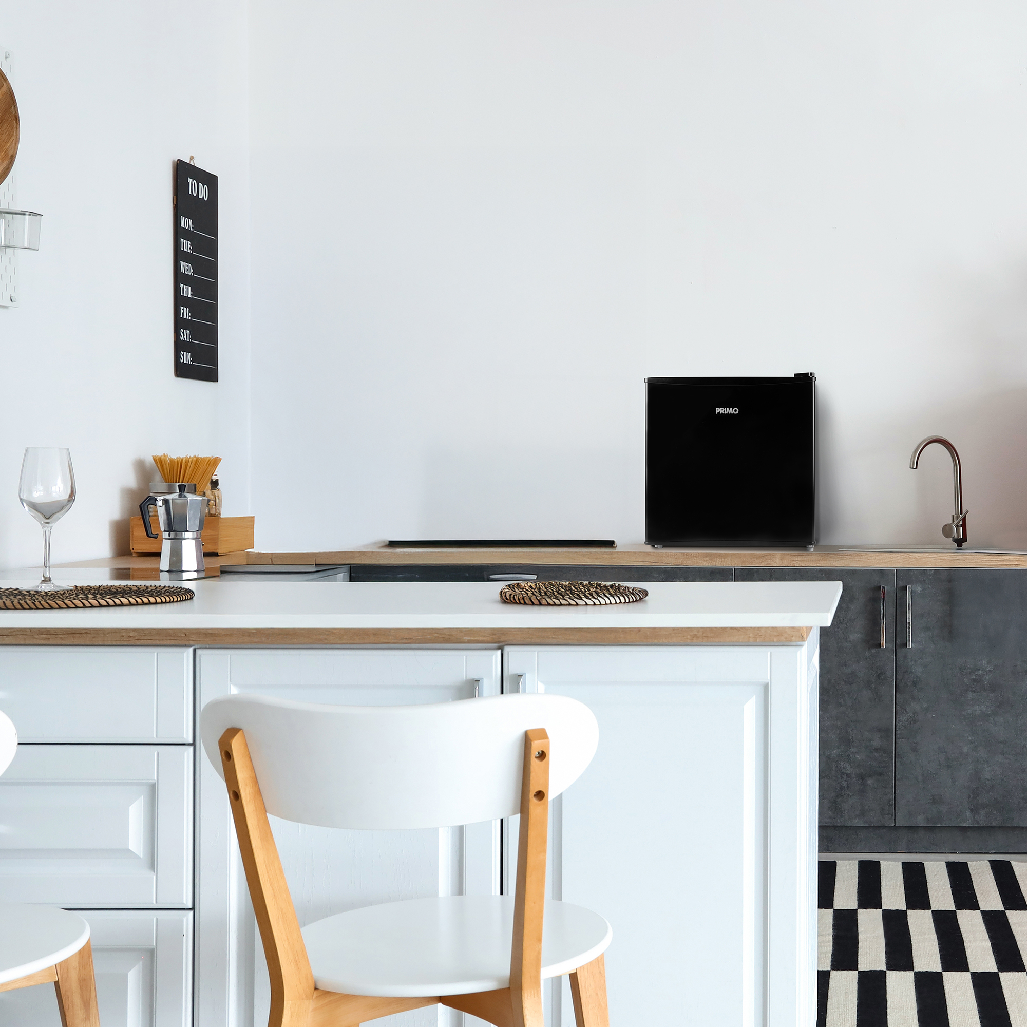 Cuisine avec un petit réfrigérateur noir, une cafetière, un verre et une liste de tâches.